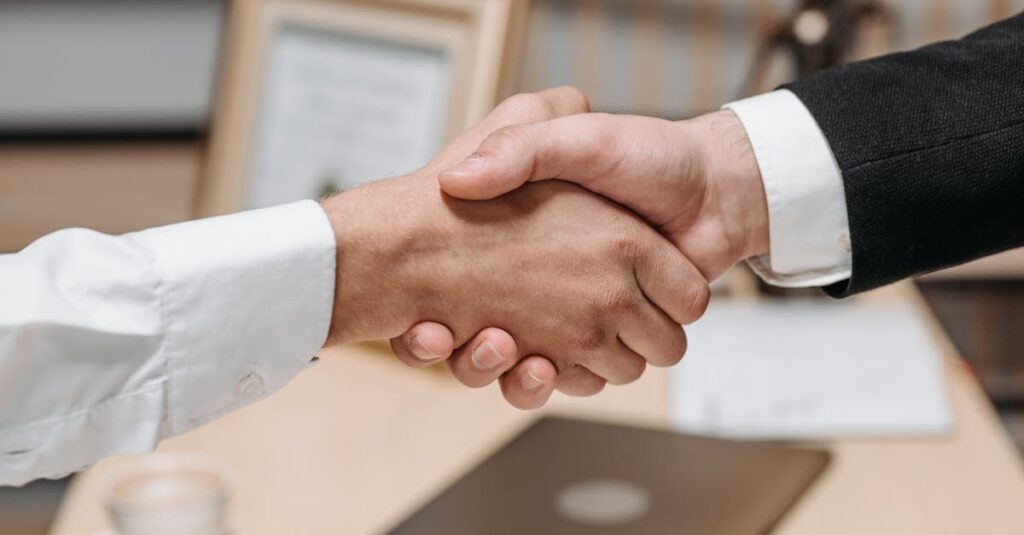 Close-up of two people shaking hands in an office, symbolizing agreement and partnership.